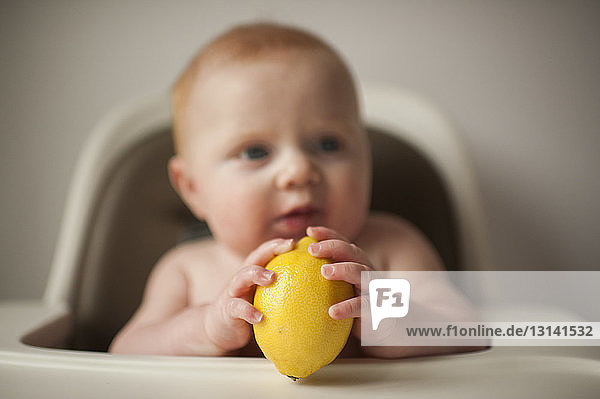 Kleiner Junge ohne Hemd  der eine Zitrone hält  während er zu Hause auf einem Hochstuhl sitzt