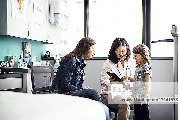 Girl using tablet computer with mother and doctor in clinic