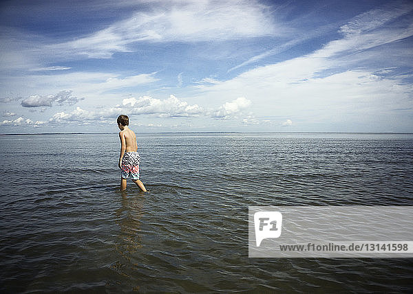 Rückansicht eines Jungen ohne Hemd  der im Meer gegen den Himmel läuft