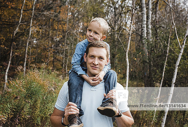 Portrait of father carrying son on shoulders while standing in forest