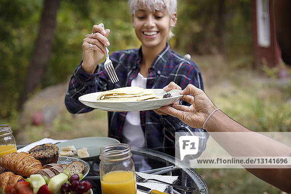 Ausgeschnittenes Bild eines Mannes  der einer jungen Frau während des Frühstücks Pfannkuchen anbietet