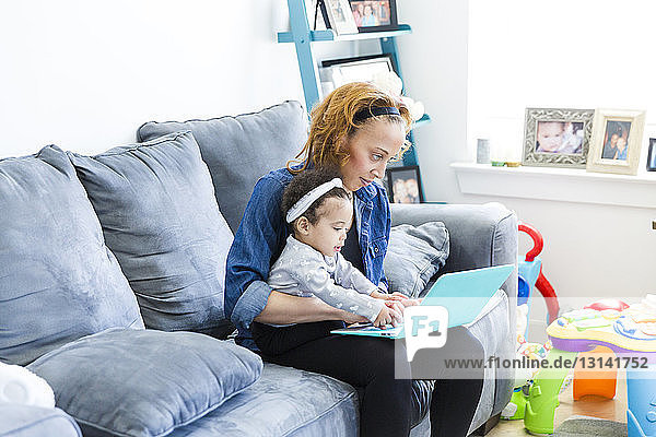 Mother and daughter using laptop computer while sitting on sofa