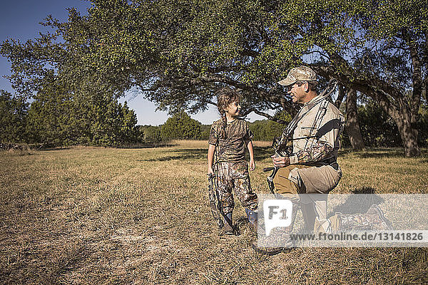 Father and daughter holding archery bows on grassy field
