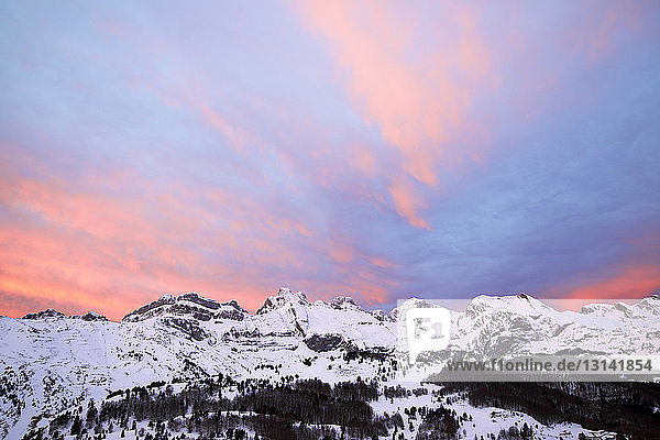 Tiefwinkel-Szenenansicht von schneebedeckten Bergen vor dramatischem Himmel bei Sonnenuntergang