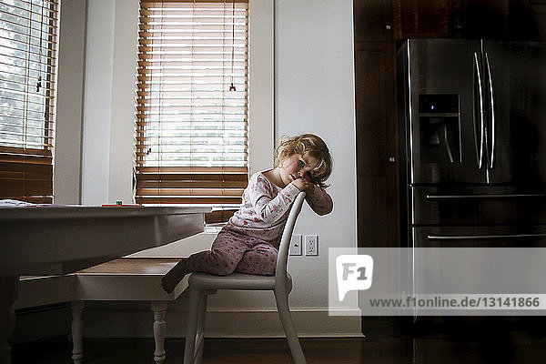Porträt eines gelangweilten Mädchens  das zu Hause auf einem Stuhl sitzt