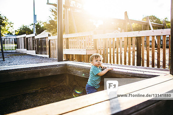 Süßer kleiner Junge  der an sonnigen Tagen an einer Holzbank auf dem Spielplatz steht