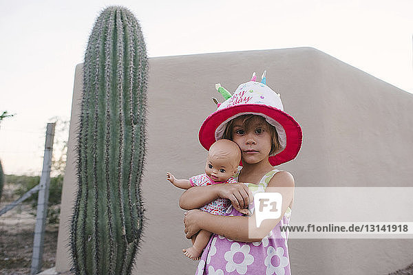 Bildnis eines Mädchens mit Hut  das eine Puppe hält  während es bei einem Kaktus steht