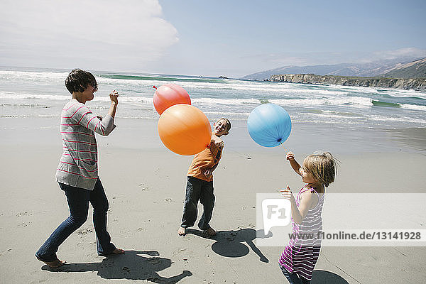 Mutter und Kinder spielen mit Luftballons  während sie am Strand im Sand stehen