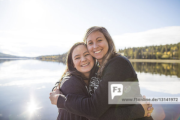 Portrait of cheerful female friends embracing against lake during sunny day