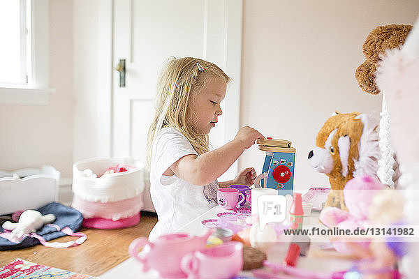 Seitenansicht eines süßen Mädchens  das zu Hause mit einem Spielzeug-Teeservice spielt