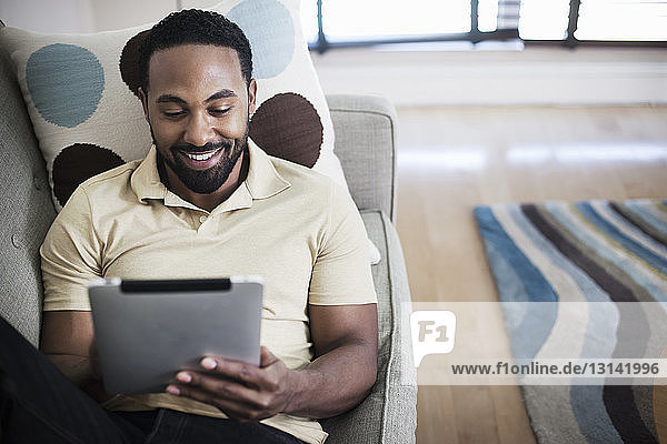 Smiling man using tablet while lying on sofa at home