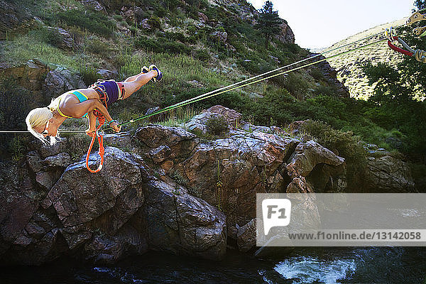 Frau balanciert auf einem Seil  während sie über einen Fluss slacklinet
