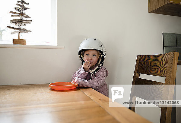 Girl wearing helmet eating food by table at home