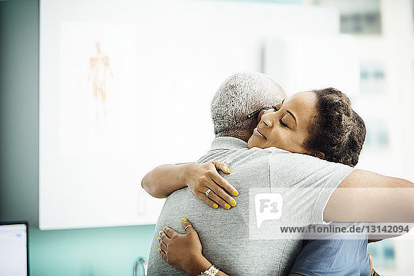 Seitenansicht einer Ärztin  die einen älteren männlichen Patienten in der Klinik umarmt