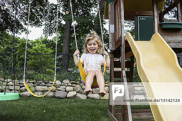 Happy cute girl swinging against trees at playground