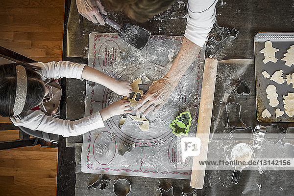 Overhead view of granddaughter and grandmother making Christmas cookies on table at home