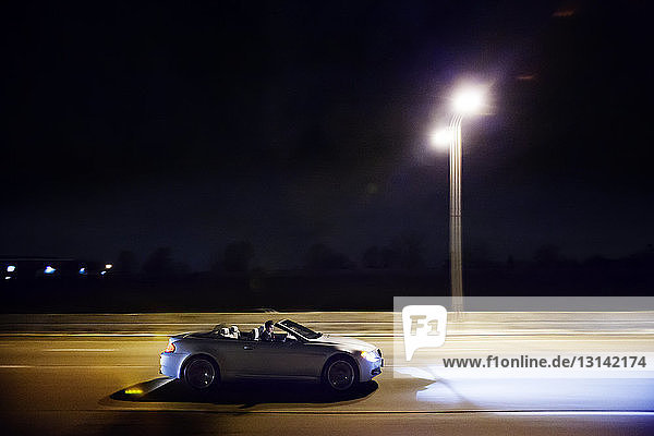 Mann fährt Auto auf beleuchteter Brücke gegen klaren Himmel bei Nacht