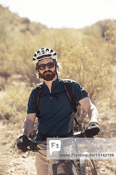 Portrait of confident biker standing with bicycle on mountain