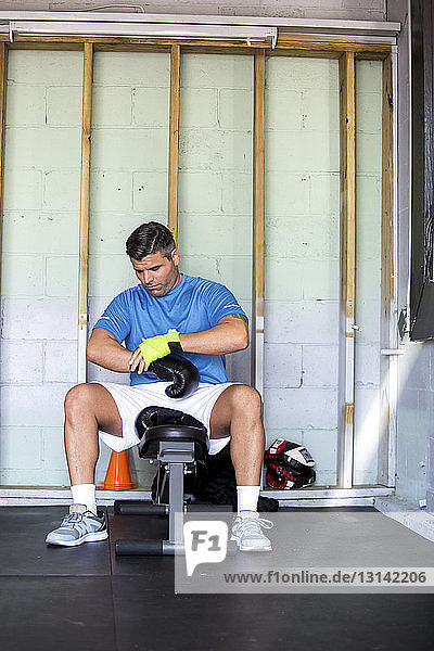 Männlicher Boxer trägt Boxhandschuhe beim Sitzen in der Turnhalle