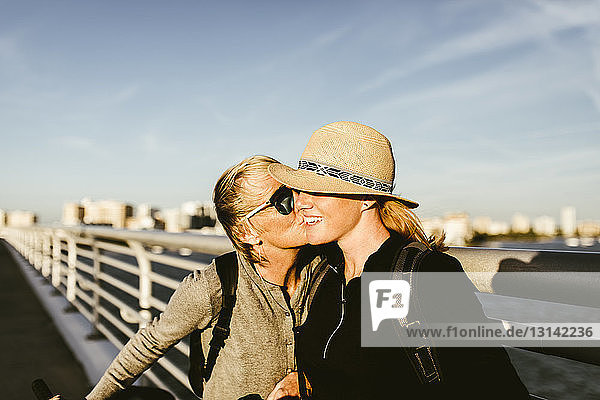 Loving mother kissing daughter on pier against sky in city