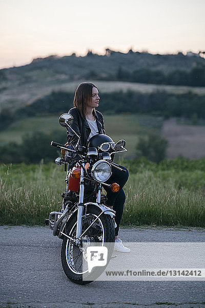 Nachdenkliche Bikerin sitzt auf Motorrad gegen Landschaft