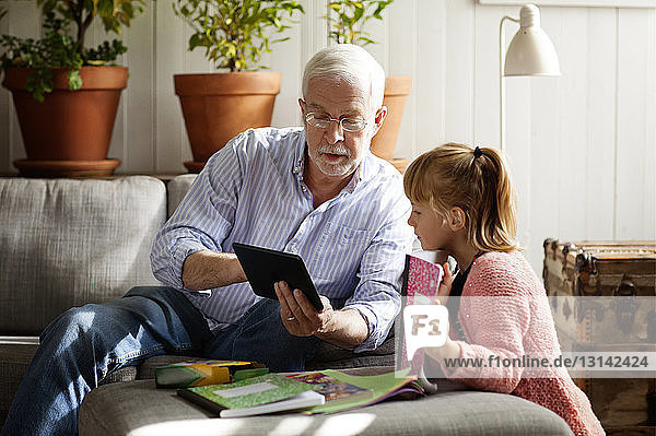Grandfather showing tablet computer to granddaughter while relaxing at home