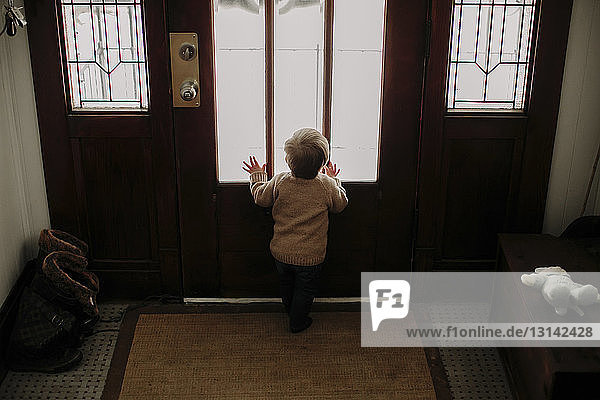 Rückansicht eines kleinen Jungen  der zu Hause durch das Glas einer Tür schaut