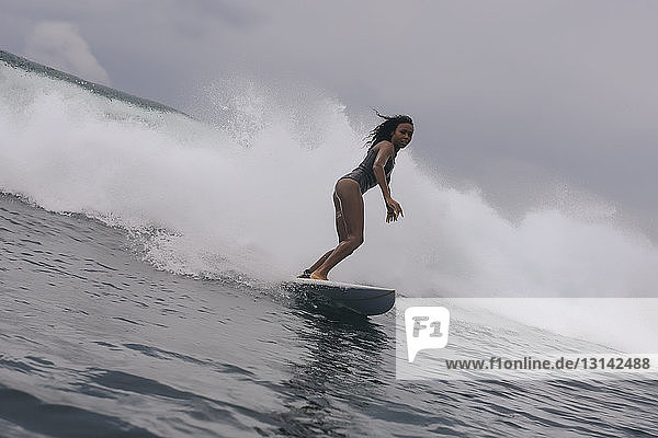 Seitenansicht einer Frau im Taucheranzug beim Surfen auf dem Meer vor bewölktem Himmel