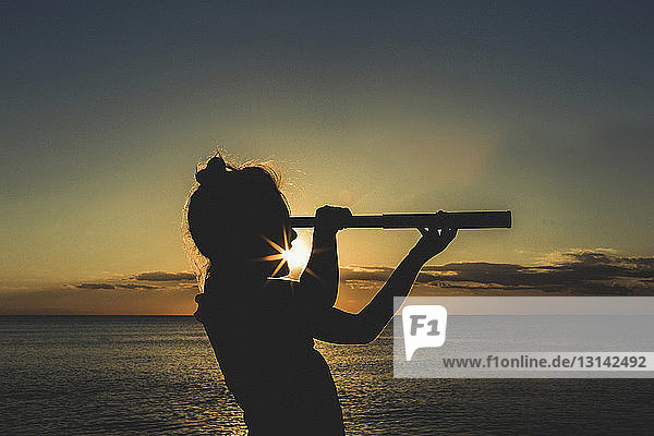 Silhouette girl using telescope against sea during sunset