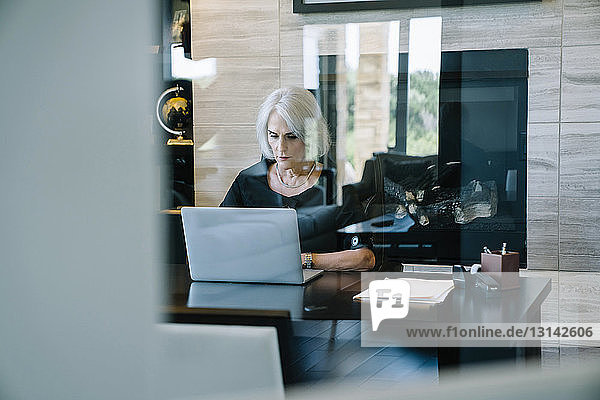 Seriöse Geschäftsfrau  die am Laptop im Büro arbeitet  durch die Tür gesehen