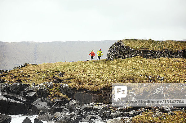 Freunde joggen auf dem Feld gegen felsige Küste