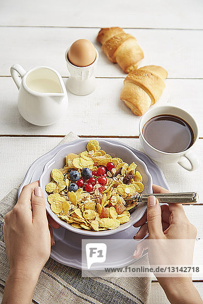 Cropped hands of woman holding bowl with breakfast cereals on table at home