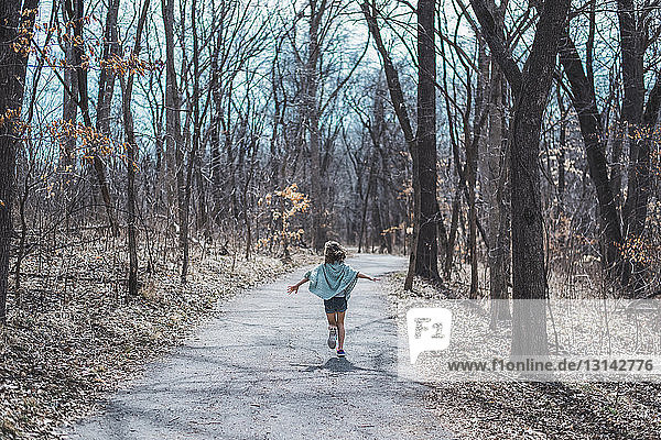Carefree girl with arms outstretched running on dirt road amidst forest