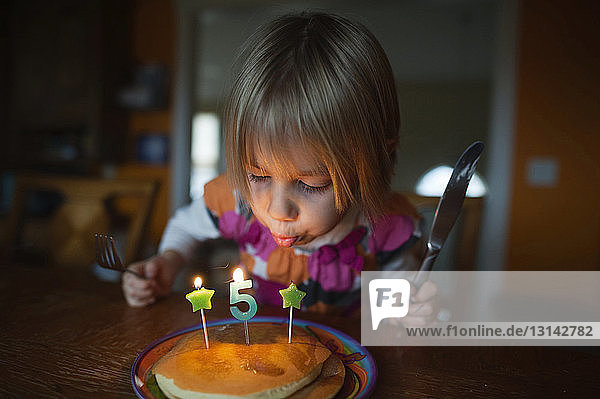 Mädchen bläst Kerzen auf Pfannkuchen