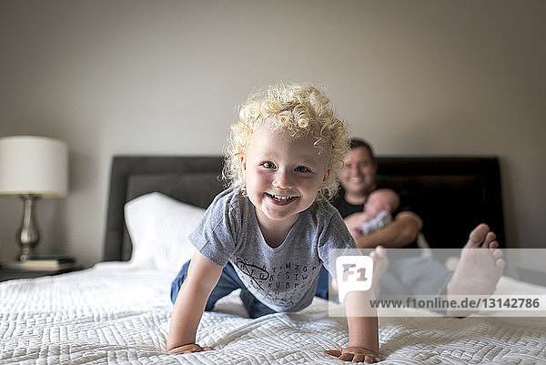 Portrait of cheerful boy with father carrying brother on bed at home