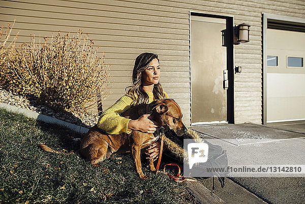 Frau mit Hund schaut weg  während sie an einem sonnigen Tag im Hof sitzt