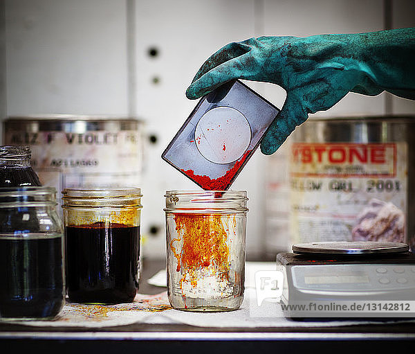 Ausgeschnittenes Bild eines Arbeiters  der bei Tisch in der Werkstatt Farbstoff in Flüssigkeit gießt