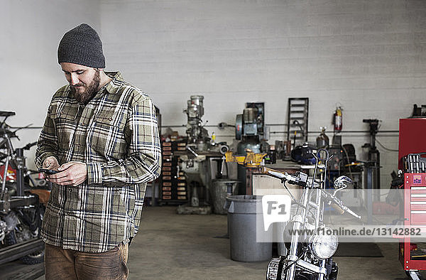 Smiling worker using phone while standing at auto repair shop