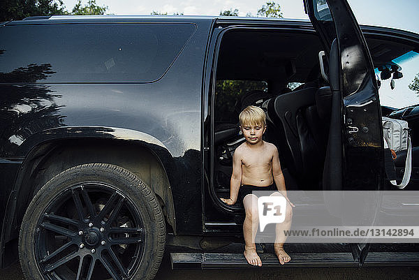 Junge ohne Hemd  der an der Autotür sitzt