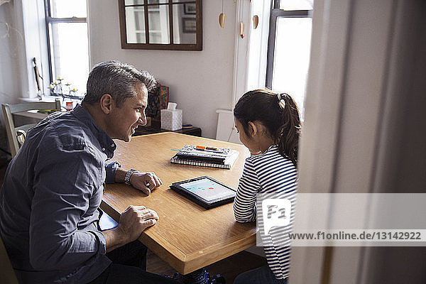 Father looking at girl using tablet computer seen through doorway