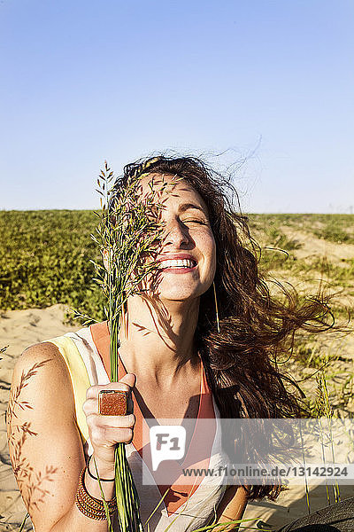 Glückliche Frau hält Pflanzen auf dem Feld gegen den klaren Himmel