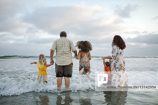 Rear view of family standing in sea at beach against cloudy sky