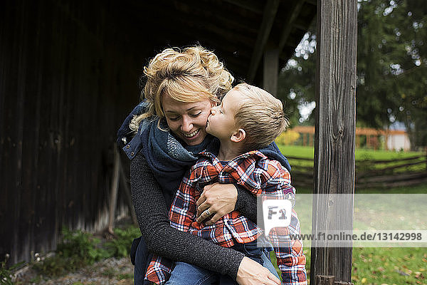 Sohn küsst lächelnde Mutter auf dem Bauernhof
