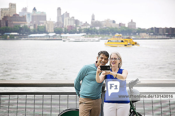 Glückliches reifes Paar  das sich beim Stehen auf der Promenade am Fluss in der Stadt Selbsthilfe leistet