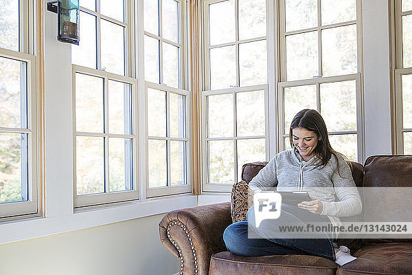 Lächelnde Frau benutzt Tablet-Computer  während sie zu Hause auf dem Sofa sitzt