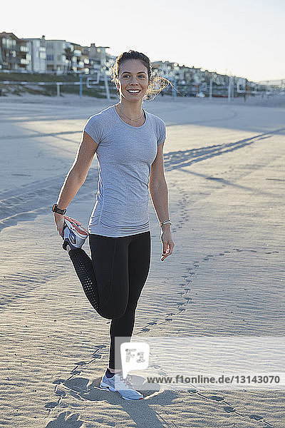 Lächelnde Frau in voller Länge mit ausgestrecktem Bein am Strand