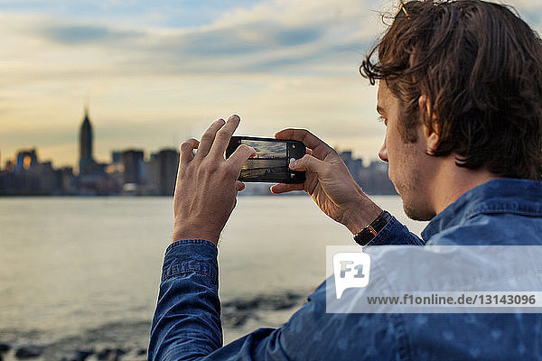Man photographing city and sea with smart phone during sunset