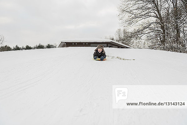 Verspielter Junge  der im Winter beim Schlittenfahren auf Schnee schreit