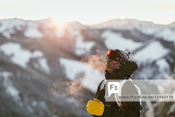 Man with backpack standing on snow covered mountain during sunset