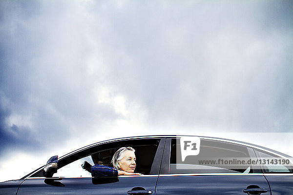 Woman looking away while sitting in car against cloudy sky